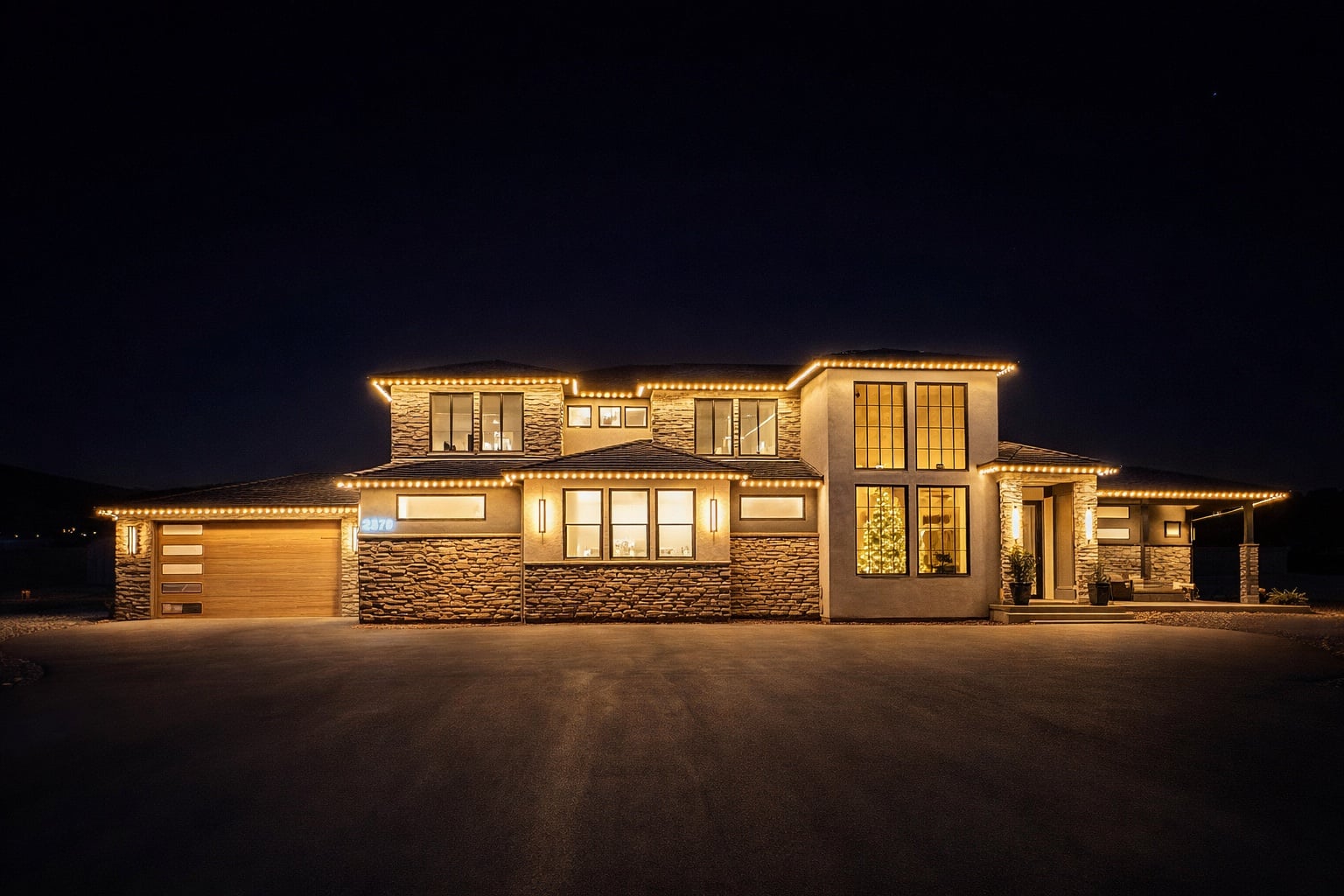 Modern stone home at night with warm gold permanent holiday lights installed by Ekko Lighting